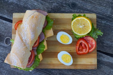 Jambonlu, peynirli, domatesli ve marullu iştah açıcı bir sandviç yumurta ve limonlu.