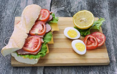 Jambonlu, peynirli, domatesli ve marullu iştah açıcı bir sandviç yumurta ve limonlu.
