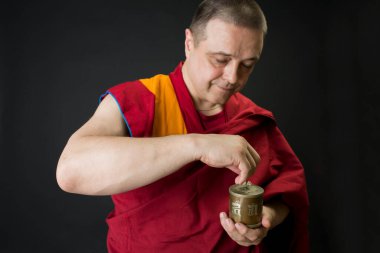 Kırmızı kesalı bir Budist keşişin portresi. Keşiş elinde bir dua davulu tutuyor.