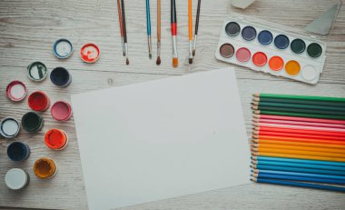 Çizim aletleri, kırtasiye malzemeleri, sanatçının çalışma yeri. Boya ve kalemler ve boş kağıtlar ahşap masa, üst görüş, düz döşeme, kopyalama alanı. okul çizim malzemeleri