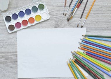 Çizim aletleri, kırtasiye malzemeleri, sanatçının çalışma yeri. Boya ve kalemler ve boş kağıtlar ahşap masa, üst görüş, düz döşeme, kopyalama alanı. okul çizim malzemeleri