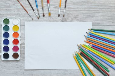 Çizim aletleri, kırtasiye malzemeleri, sanatçının çalışma yeri. Boya ve kalemler ve boş kağıtlar ahşap masa, üst görüş, düz döşeme, kopyalama alanı. okul çizim malzemeleri