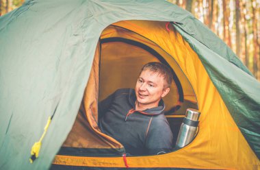 Adam ormanda çadırın yanında oturuyor.