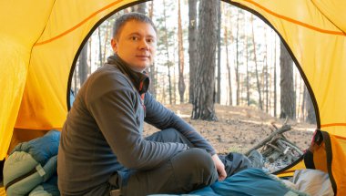 Adam ormanda çadırın yanında oturuyor.