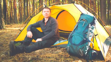 Adam ormanda çadırın yanında oturuyor.