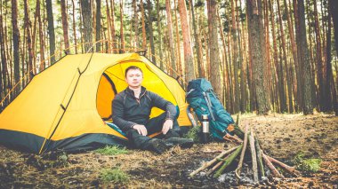 Adam ormanda çadırın yanında oturuyor.