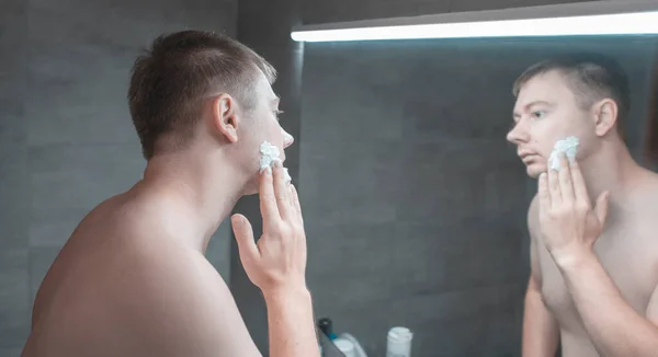 Guy puts shaving gel on his face