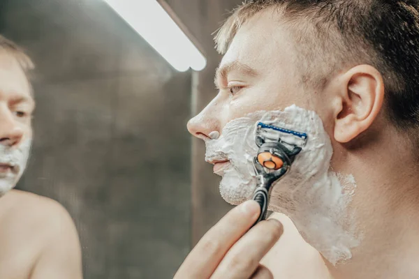 Adam banyo aynasının yanında tıraş oluyor. Elinde bir jiletle