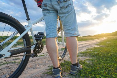 Dağ bisikletli bir adam gün batımında toprak bir yola çıkıyor.