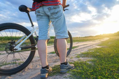 Dağ bisikletli bir adam gün batımında toprak bir yola çıkıyor.