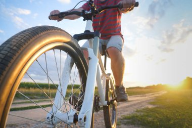 Dağ bisikletli bir adam gün batımında toprak bir yola çıkıyor.