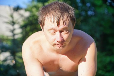 Adam bahçede soğuk suyla yıkanıyor.