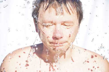 Adam yüzünü suyla yıkıyor, damlalar farklı yönlere uçuyor, beyaz bir arka planda.
