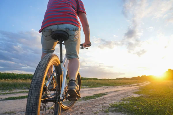 A guy on a mountain bike rides a dirt road at sunset