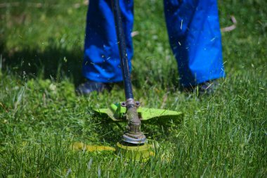 Bir adam evinin yanında elektrikli çim biçme makinesiyle çim biçiyor.