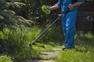 Bir adam evinin yanında elektrikli çim biçme makinesiyle çim biçiyor.