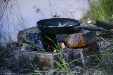 Tavadaki balık nehir kıyısında bir ateşte kızarır. Nehir kenarında akşam yemeği ve kazıkta yemek.