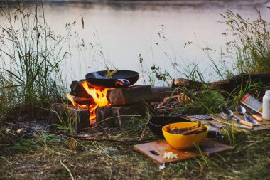 Tavadaki balık nehir kıyısında bir ateşte kızarır. Nehir kenarında akşam yemeği ve kazıkta yemek.