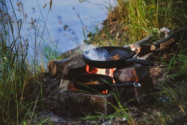 Tavadaki balık nehir kıyısında bir ateşte kızarır. Nehir kenarında akşam yemeği ve kazıkta yemek.