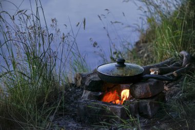 Tavadaki balık nehir kıyısında bir ateşte kızarır. Nehir kenarında akşam yemeği ve kazıkta yemek.