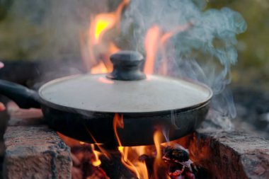 Kızarmış et sosisi, ateşin yanındaki tavada uzanmak.