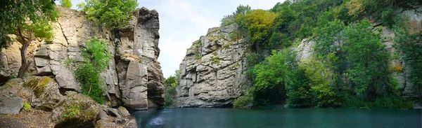 panorama of large stone rocks with a river between them with clear water. Trees grow on the rocks.