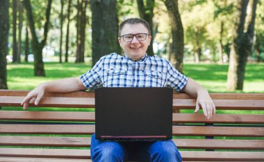 Dizüstü bilgisayarı olan bir adam bankta oturuyor..