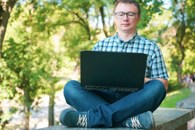 Adam parkta oturuyor ve dizüstü bilgisayarda çalışıyor..