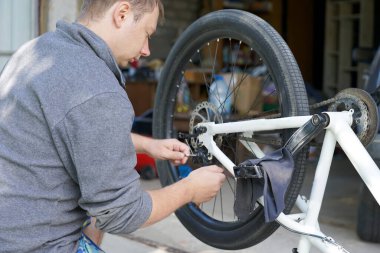 Bisikletli adam motosikletin yanına oturur ve arka disk frenini ayarlar.