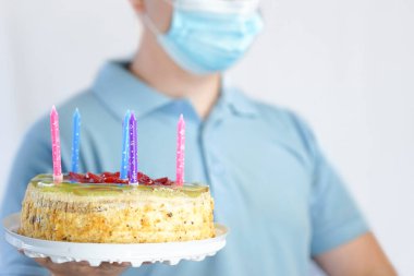 Maskeli adam elinde bir pasta tutuyor. Covid-19 karantinasında doğum günü kutlaması
