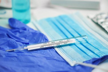 Bir cıva termometresi maske ve eldivenlerin üzerinde yatar.