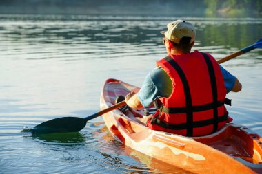 Adam can yeleği giyiyor ve bir şapka bir kanonun içinde gölde yüzüyor. Sis gölün üzerinde yükseliyor.