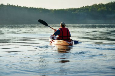 Adam bir kakyak 'ın içinde gölde yüzüyor. Sis gölün üzerinde yükseliyor.