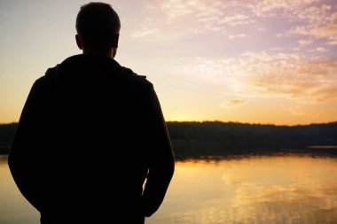 Gölün kenarında durup gün batımını izleyen bir adamın silueti.