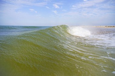 Beyaz tepeli gök mavisi bir deniz dalgası kıyıya vuruyor..