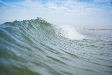 Beyaz tepeli gök mavisi bir deniz dalgası kıyıya vuruyor..
