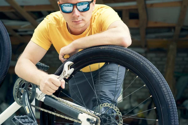 戴眼镜的人拿着可调扳手修理 站在自行车旁边 — 图库照片