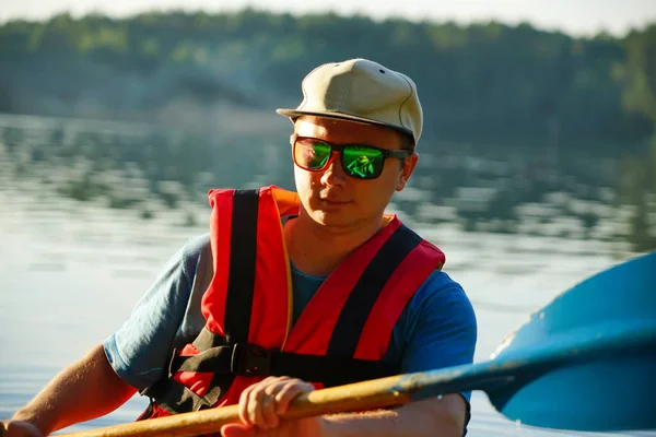 a guy in a life jacket holds a paddle in his hands while sleeping on a canoe