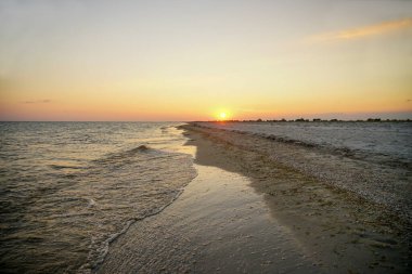 Deniz kenarında turuncu güneşli gün batımı. Dalga kıyıya vuruyor.