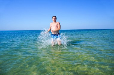 Adam denizdeki dalgalar boyunca masmavi suyla koşuyor. Sıçramalar yanlardan uçar.