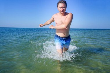 Adam denizdeki dalgalar boyunca masmavi suyla koşuyor. Sıçramalar yanlardan uçar.