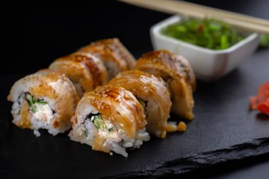 Yılanbalıklı suşi ve saman Wakamei salatası taş levhadan yapılmış siyah bir tahtada yatıyor.