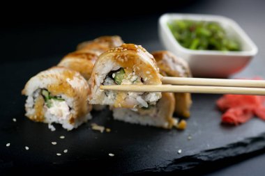 Bir el, Çin yemek çubuklarıyla yılan balığı suşisi rulosunu tutuyor.