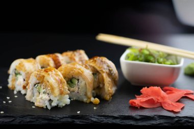 Yılanbalıklı suşi ve saman Wakamei salatası taş levhadan yapılmış siyah bir tahtada yatıyor.