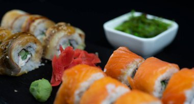 Suşi seti rulo yılan balığı, somon ve hayashi wakame salatası kayrak taşından yapılmış siyah bir tahtanın üzerinde yatıyor.