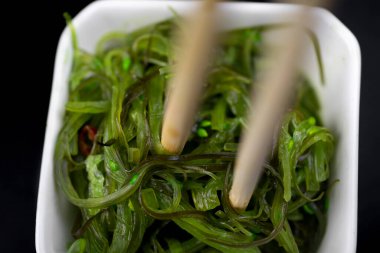 Siyah arka planda beyaz tabakta yemek çubuklarıyla salata.