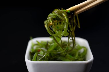 Siyah arka planda beyaz tabakta yemek çubuklarıyla salata.