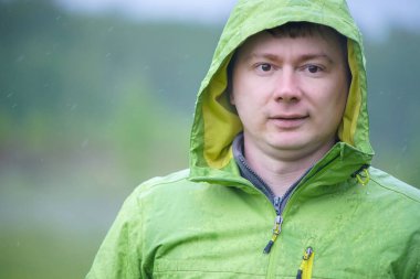 Yağmurluklu genç bir adam yağmurda duruyor. Yüzüne ve ceketine yağmur damlaları düşer..