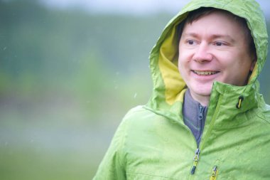 Yağmurluklu genç bir adam yağmurda duruyor. Yüzüne ve ceketine yağmur damlaları düşer..