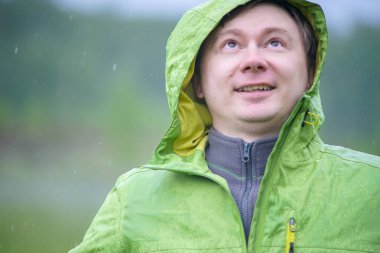 Yağmurluklu genç bir adam yağmurda duruyor. Yüzüne ve ceketine yağmur damlaları düşer..